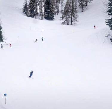 Skier carving down a wide, sunny ski slope in an Austrian ski resort. High, snow-capped mountain pea