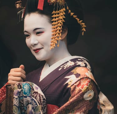 portrait of a smiling geisha or maiko (apprentice) wearing a dark purple kimono with a colorful patt