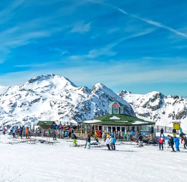 Group of people enjoying a sunny day at the summit of an Austrian ski resort. Scenic view of mountai