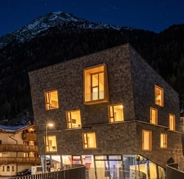 A modern, geometrically designed building with illuminated windows at night, situated in a snowy ski