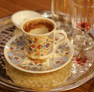 a cup of coffee on a tray with a spoon and a glass of wine