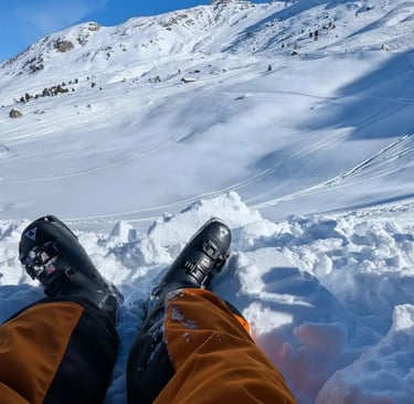 Relaxed skier sitting with boots stretched out, overlooking snowy alpine mountains
