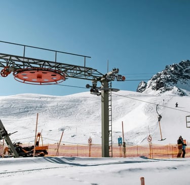 A snowy mountain scene featuring ski lift infrastructure and slopes. The foreground shows part of th