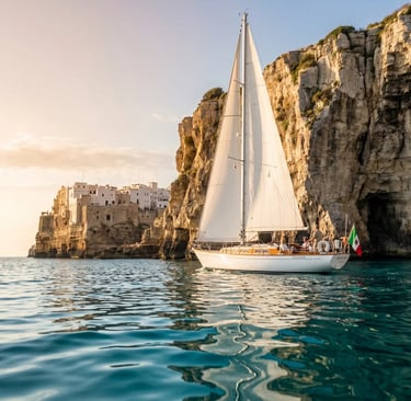 Classic white sailboat sailing near Polignano a Mare limestone cliffs at sunset