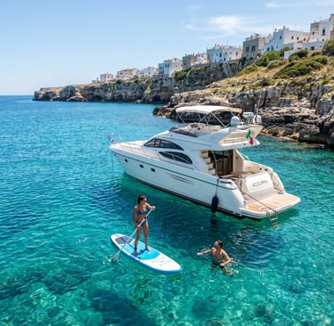 Luxury yacht anchored near Polignano a Mare cliffs with woman on SUP board and swimmer in sea