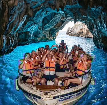 Tourists in life vests taking identical phone photos inside blue sea cave on Polignano boat tour