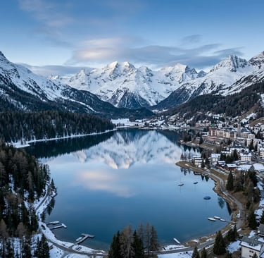  Drone shot of St. Moritz lake reflecting snowcapped peaks with alpine village on the shore