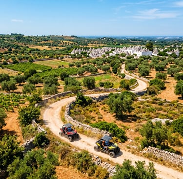 Aerial view of two buggies on winding dirt trail through Itria Valley with trulli in background