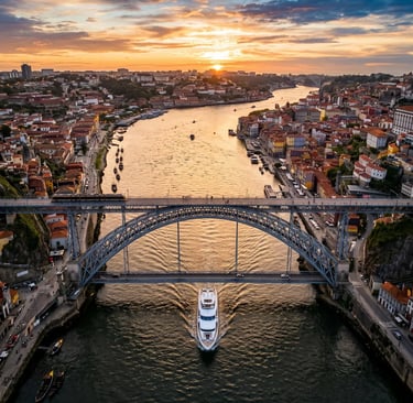 Aerial view of a yacht passing under Dom Luís Bridge on the Douro River at sunset.
