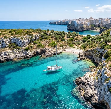 Aerial view of white sailboat anchored in turquoise cove near Polignano a Mare
