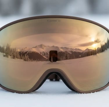 Close up of ski goggles with amber lens and brown strap reflecting snowy mountains and sunset.