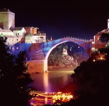 Mostar Old Bridge lit with colorful lights reflecting on Neretva River at night