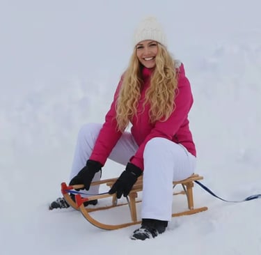 Blonde woman on a wooden sled enjoying the snow with mountain views in Grindelwald, Switzerland.