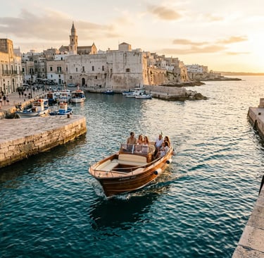 Wooden private boat with guests leaving Monopoli old town harbor at golden hour sunset in Puglia