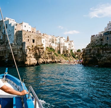 Blue wooden boat approaching whitewashed Polignano a Mare cliffs and Lama Monachile beach.