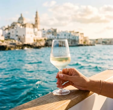 Hand holding white wine glass on boat with Monopoli skyline behind
