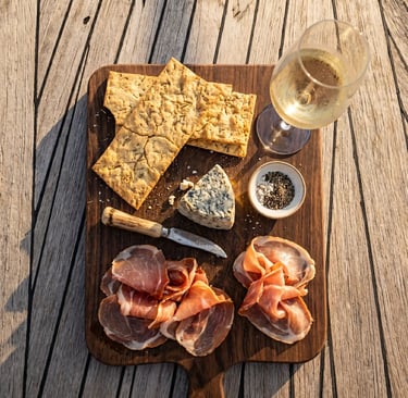 Overhead view of rosemary crackers, cheese, cured meat and white wine on yacht deck