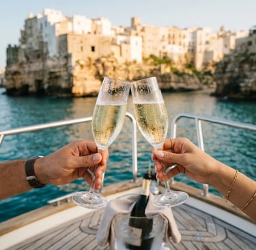 Couple toasting with chilled prosecco glasses on boat deck with Polignano a Mare cliffs behind