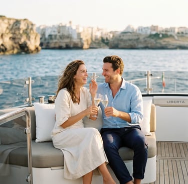 Couple toasting prosecco on luxury yacht Libertá with Polignano a Mare cliffs in background