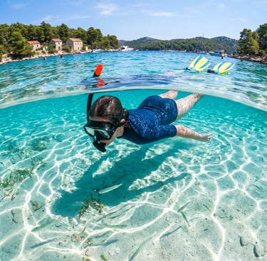 Underwater split shot of snorkeler gliding over sandy bottom in turquoise Croatian bay