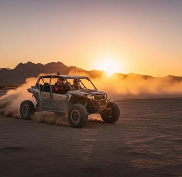 Person driving an off-road ATV through a sandy desert at sunset, kicking up dust.
