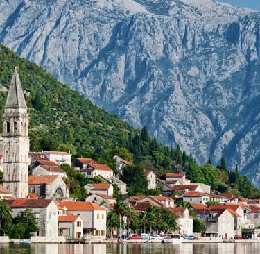Stone village of Perast reflected in calm bay water with snow-capped mountains behind
