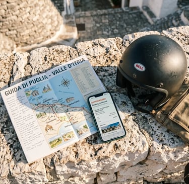 Valle d'Itria travel map, GetYourGuide booking on smartphone, and buggy helmet on limestone wall