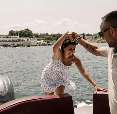 Boat skipper assisting smiling woman in summer dress boarding tour boat in Monopoli harbor