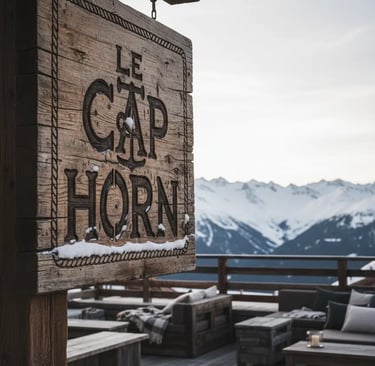 A rustic wooden sign for Le Cap Horn restaurant with snow-capped mountain peaks of Courchevel in the