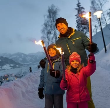 A father and his two children smiling while holding lit torches during a family-friendly night hike 