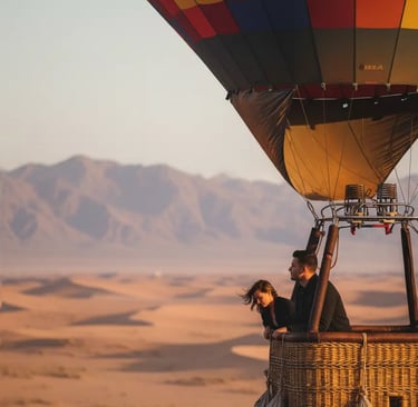 Couple in a hot air balloon floating over a desert landscape at sunrise.