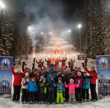 A large group of people posing for a photo on a snowy ski slope at night, holding torches with a lit