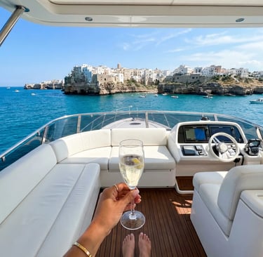 Flybridge view of Polignano a Mare with prosecco glass, white leather seating and teak deck