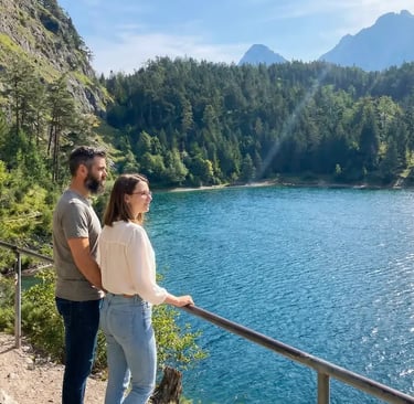 Couple standing at viewpoint railing overlooking turquoise Drachensee lake surrounded by pine forest
