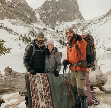 Three hikers posing with a colorful blanket at frozen Emerald Lake in winter.
