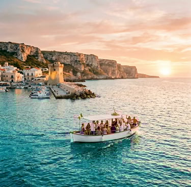 White tour boat leaving Torre Vado seafront at golden hour with cliffs and tower in background.