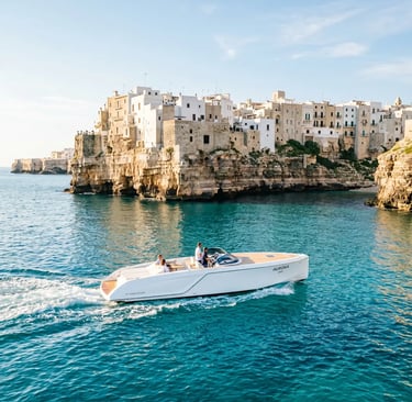 Luxury private boat sailing past Polignano a Mare whitewashed cliffside village on Adriatic coast