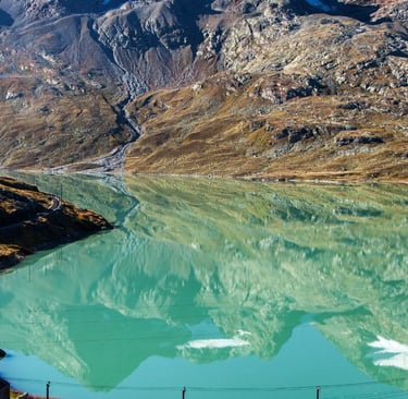 Red Bernina Express train passing turquoise alpine lake with mountain reflections