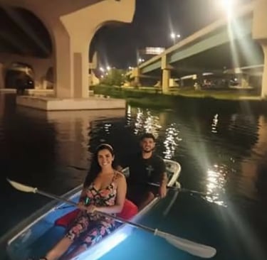 Couple enjoying a romantic date night in a clear kayak with blue glow lights during a bioluminescent
