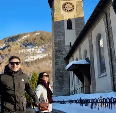 Tourists walking past the historic church tower in Zermatt village center as part of a cultural walk