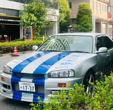 Silver Nissan Skyline R34 GT-R replica driving on Tokyo streets.