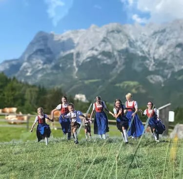Children in traditional outfits running through a green Alpine meadow.