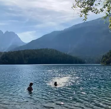 Couple swimming in calm alpine lake with sunlit mountain backdrop and forested hills in Tyrol