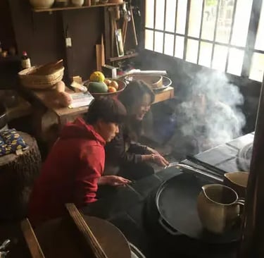 Two people cooking over an open hearth in a rustic Japanese farmhouse kitchen