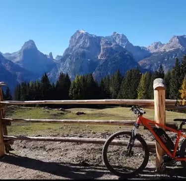 Orange e-bike at wooden fence with dramatic Dolomite peaks in autumn background
