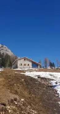  Traditional stone alpine rifugio in the Dolomites with snow patches and blue sky