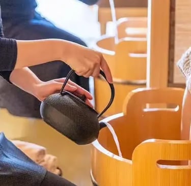 Cast iron kettle pouring warm water into wooden foot bath tub at Japanese spa