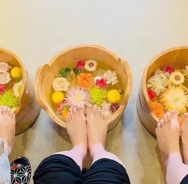 Three people soaking feet in wooden tubs filled with colorful flower petals at Kyoto spa