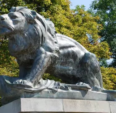 Bronze lion sculpture at Schlossberg Graz surrounded by green trees