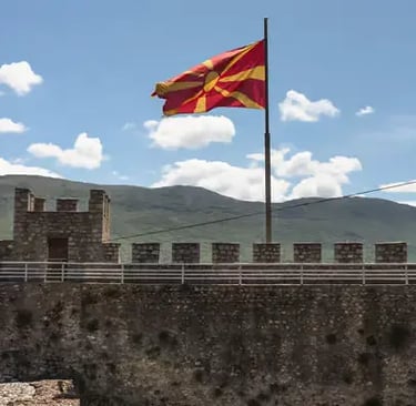 North Macedonia national flag waving on stone fortress walls with mountains and blue sky Ohrid